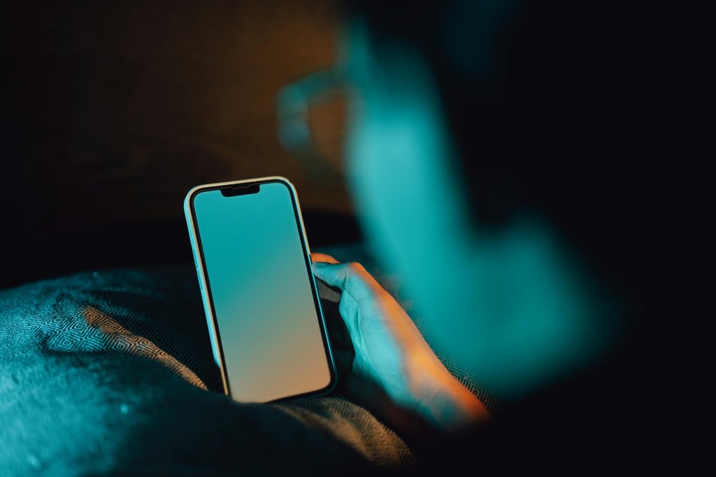 A man holding a smartphone with a blank screen in a dark room, creating a moody ambiance.